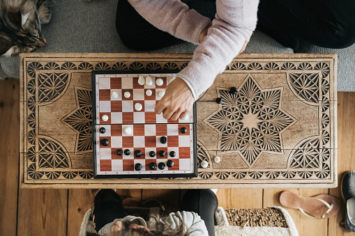 overhead view on female and childs hand playing chess on wooden bench in living room
