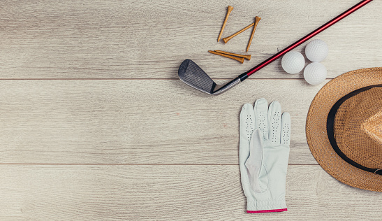 Golf club, tee's, golf balls, golf glove and hat on wooden table background. Flat lay concept. No people.