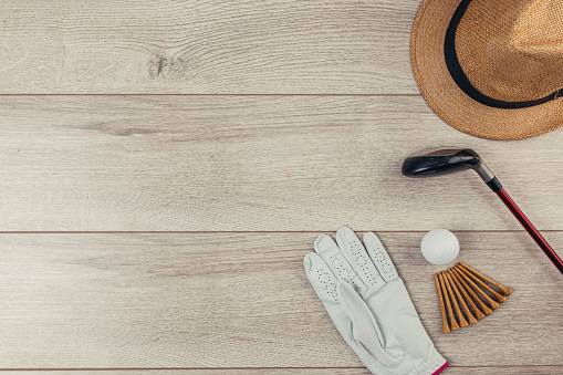 Golf club, tee's, golf balls, golf glove and hat on wooden table background. Flat lay concept. No people.