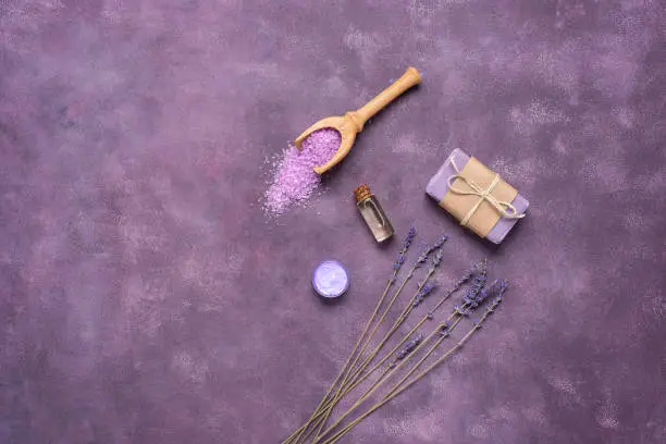 Lavender spa products on an on purple grunge background. Body care products with lavender-oil, salt, cream, soap and dried lavender flowers. Selective focus