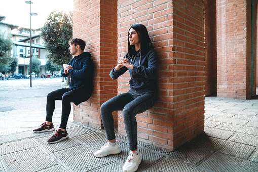 Young adult couple exercising together outdoor in the city. They are in squatting position.