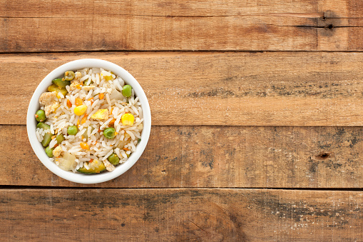 Top view of white bowl full of white rice with egg and vegetables salad over wooden table
