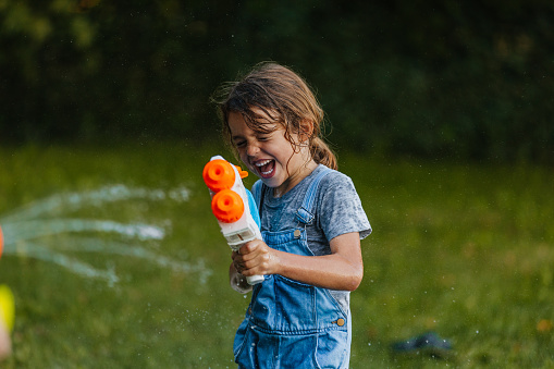 Portrait of a preschool aged girl being splashed by squirt gun outdoors.