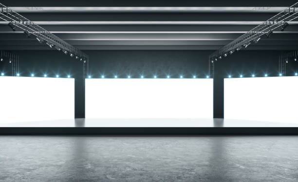 istock Blank glowing white screens in empty exhibition hall with black podium, dark concrete floor and lights on top. Mock up 1306542876