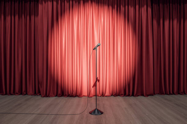 Speaker performance concept with round spotlight on red curtain and microphone on wooden floor of empty stage. 3D rendering