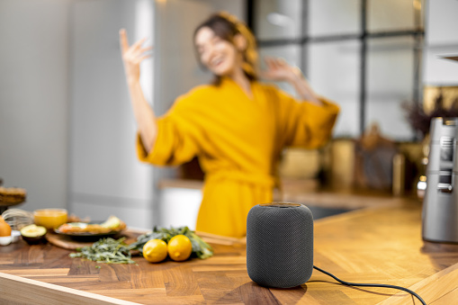 Happy woman dancing on the kitchen during a breakfast time, listening to the music from a smart speaker at home