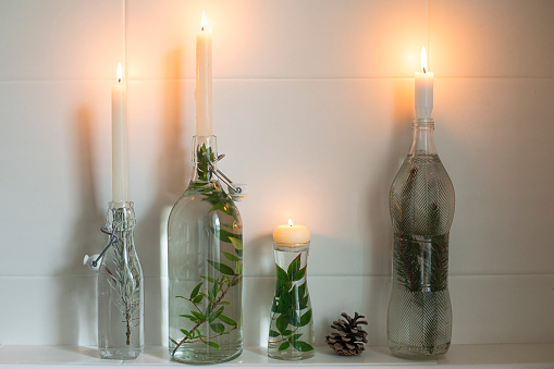 Candles in bottles filled with water and greenery, natural and simple home decor idea for Christmas.