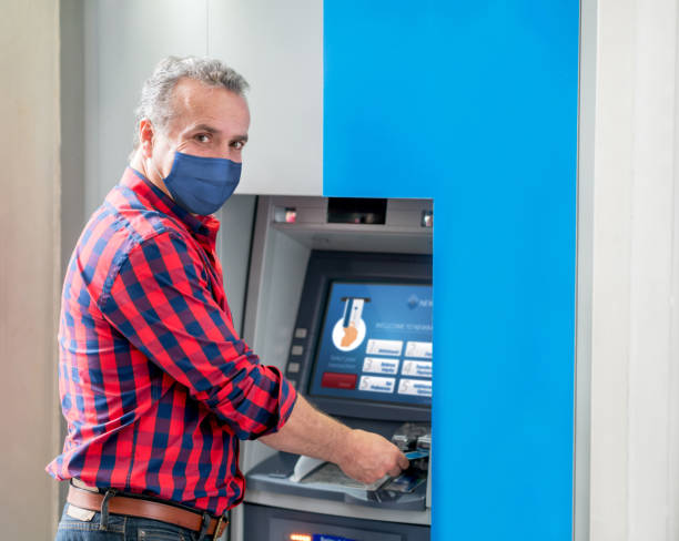 istock Man withdrawing money from an ATM wearing a facemask 1306550170