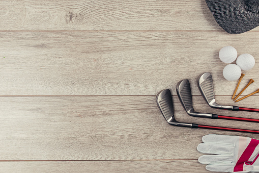 Golf clubs, tee's, golf balls, golf glove and hat on wooden table background. Flat lay concept. No people.