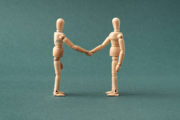 istock Two wooden figures shaking hands on a blue background - agreement or friendship concept 1306551755