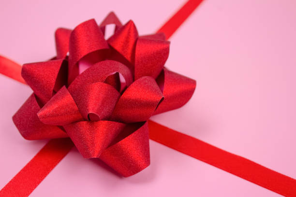 Close up of composition with decorative red ribbon bow on pink background with copy space for text. Giving presents, holidays sale or giveaway concept. Greeting card design, selective focus