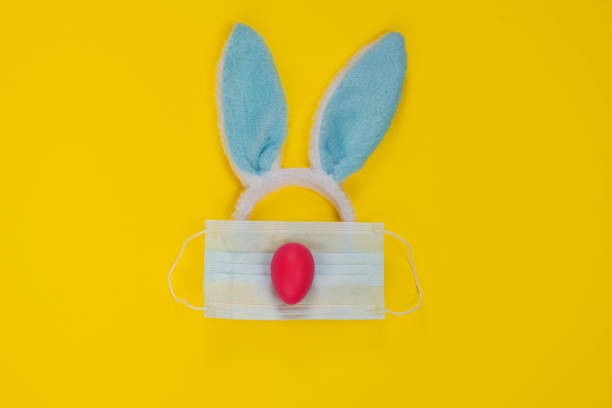 istock Happy Easter during the Coronavirus Time! Rabbit Blue Ears, Face Mask and Pink Egg on Yellow background. 1306553051