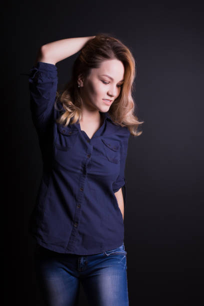 schönes junges model mit langen lockigen haaren trägt hemd und jeans, posiert auf schwarzem hintergrund - 6006 stock-fotos und bilder