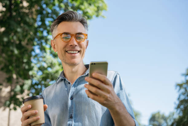 istock Stylish mature man using mobile phone, holding coffee 1306561632