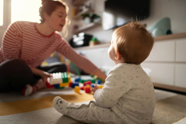 hintergrundansicht eines kleinen jungen, der auf dem boden sitzt, spaß mit spielzeug hat und seine mutter anschaut - child playroom parent indoors stock-fotos und bilder