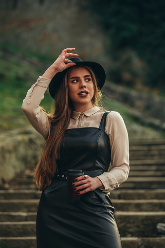 Cropped shot of a fashionable young woman posing outside while wearing a hat and a leather dress