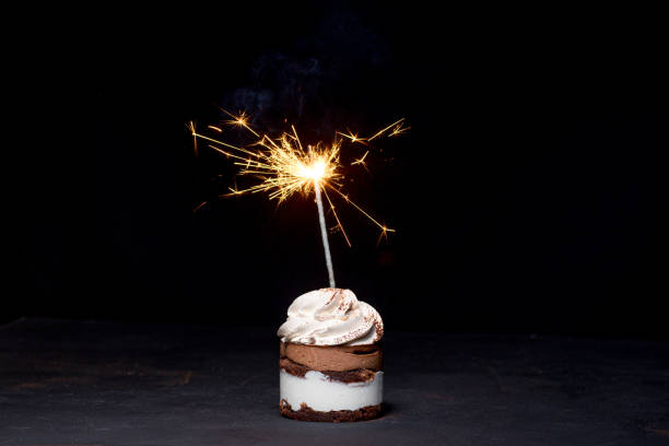 istock Delicious birthday cupcake with firework candle on table against dark background. 1306567812