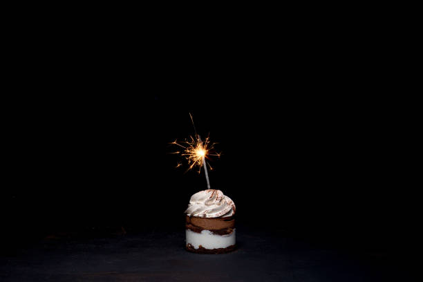 istock Delicious birthday cupcake with firework candle on table against dark background. 1306567820