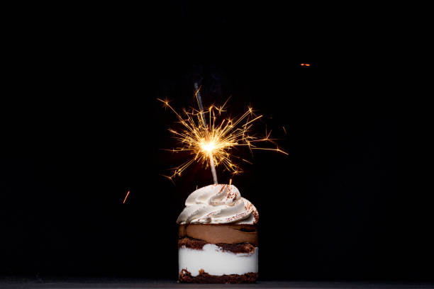 istock Delicious birthday cupcake with firework candle on table against dark background. 1306567823