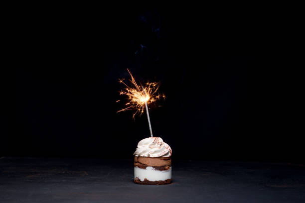 istock Delicious birthday cupcake with firework candle on table against dark background. 1306567827