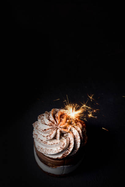 istock Delicious birthday cupcake with firework candle on table against dark background. 1306567828