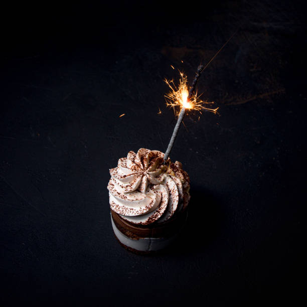 istock Delicious birthday cupcake with firework candle on table against dark background. 1306567830