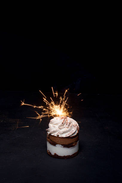 istock Delicious birthday cupcake with firework candle on table against dark background. 1306567836