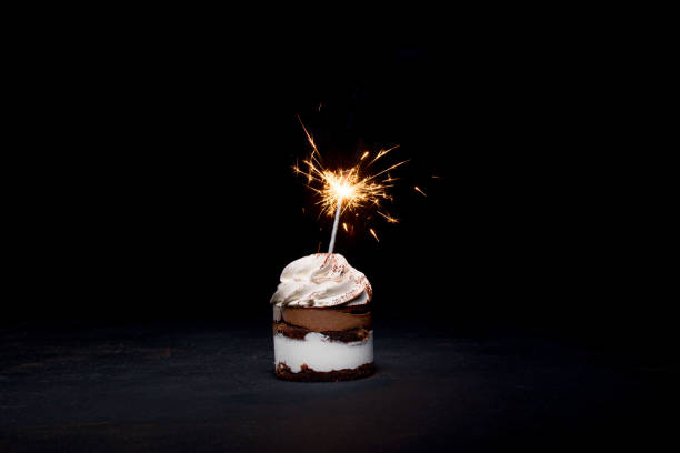 istock Delicious birthday cupcake with firework candle on table against dark background. 1306567837