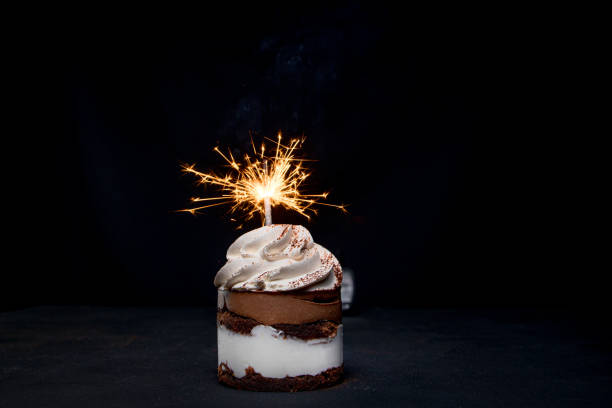 istock Delicious birthday cupcake with firework candle on table against dark background. 1306567843