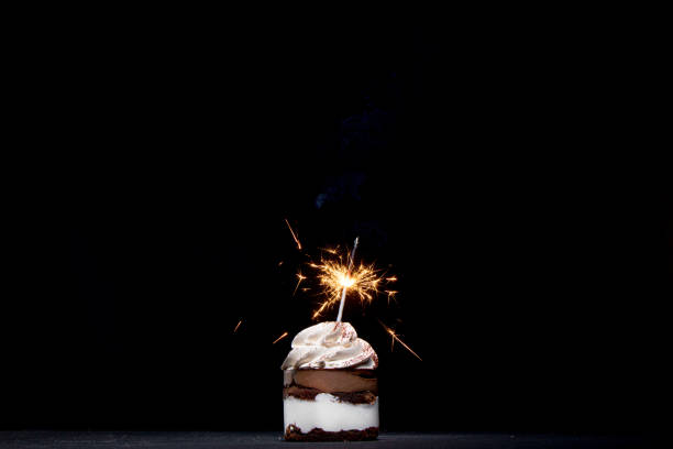 istock Delicious birthday cupcake with firework candle on table against dark background. 1306567847