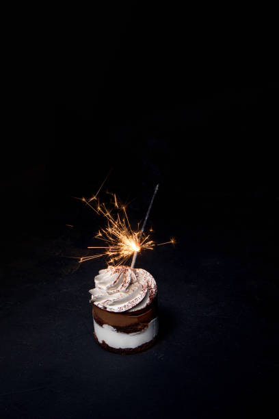 istock Delicious birthday cupcake with firework candle on table against dark background. 1306567861