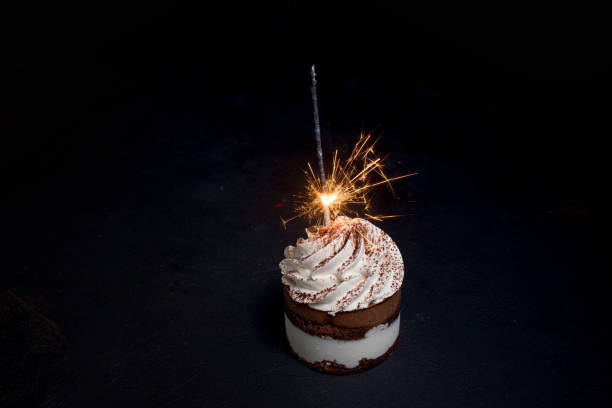 istock Delicious birthday cupcake with firework candle on table against dark background. 1306567869