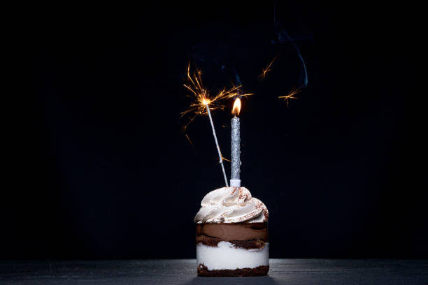 istock Delicious birthday cupcake with firework candle on table against dark background 1306567922