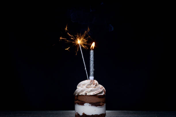 istock Delicious birthday cupcake with firework candle on table against dark background 1306567927