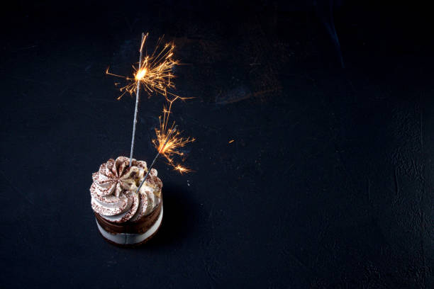 istock Delicious birthday cupcake with firework candle on table against dark background. 1306567990