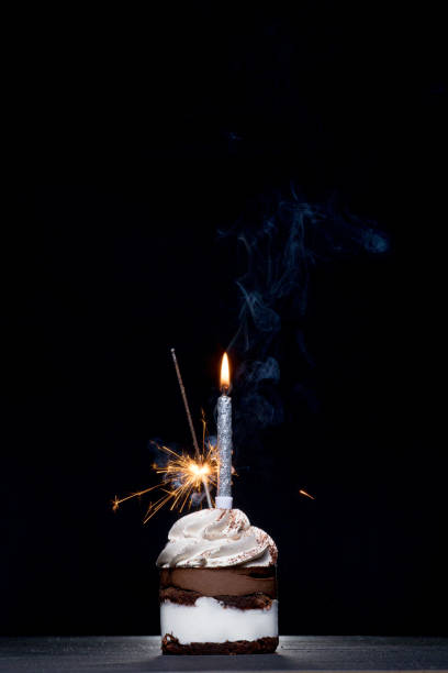 istock Delicious birthday cupcake with firework candle on table against dark background 1306568005