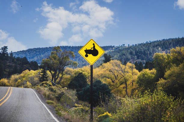 Mountain road  with ridge and fall trees in background and caution sign displaying man on tractor.j