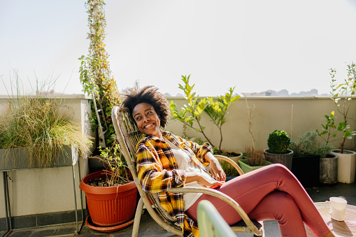 Photo of a young woman sitting and enjoying the tranquility of her lovely rooftop urban garden, on a bright spring morning.
