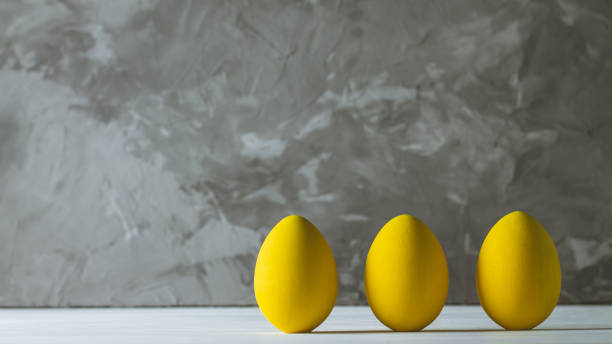 fila de cinco huevos de pascua amarillo brillante, de pie sobre la superficie de madera blanca sobre fondo de hormigón gris. copiar espacio - colores fotos fotografías e imágenes de stock