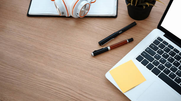 istock Computer laptop, pens, head phone and notebook on wooden office desk. 1306592748