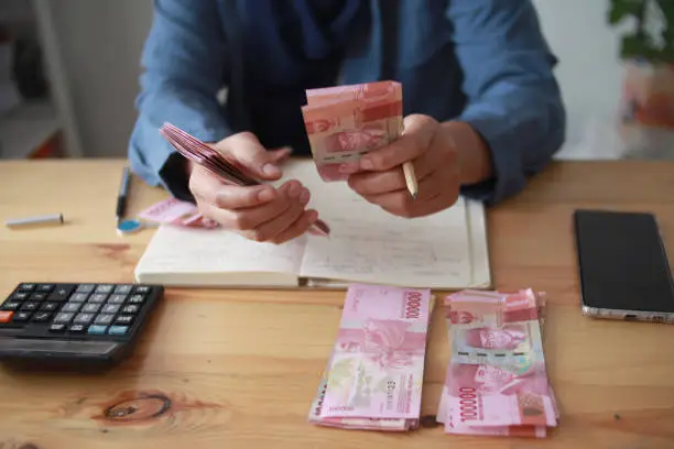 Photo of Close up of woman hand counting money uang Indonesian rupiah and making notes, money financial management