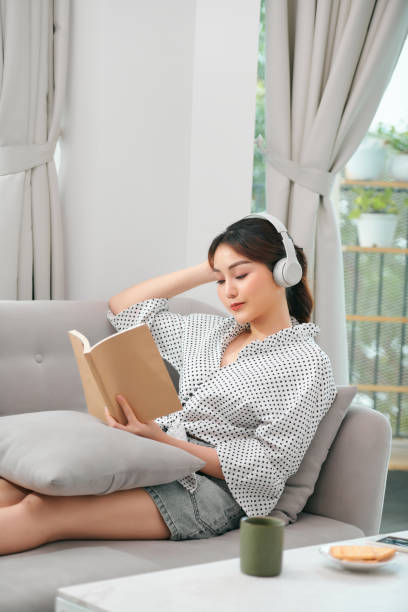istock Young relaxed woman on sofa with headphones reading a book 1306604736