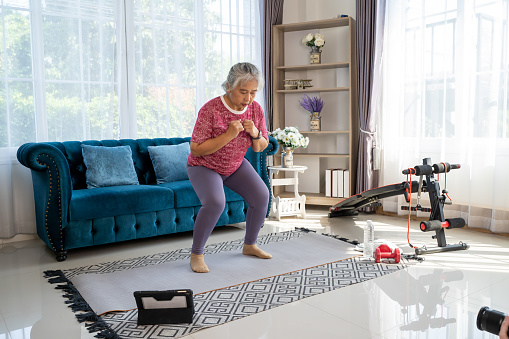 Senior woman exercise with squat pose, she watch laptop for Training exercise online In Living Room During Quarantine