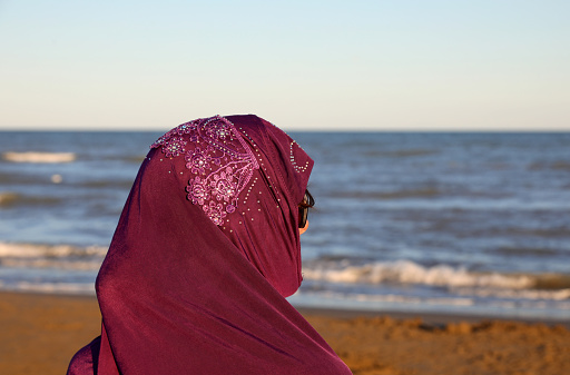 chica con velo árabe para cubrirse la cabeza junto al mar al atardecer photo