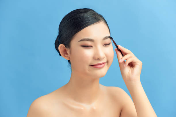 istock Beautiful young woman applying eyebrow brush on blue 1306622863