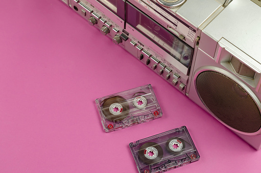 Boombox Stereo Radio Cassette Recorder and random cassettes on pink background. Vintage Cassette Deck,  retro technology, selective focus.