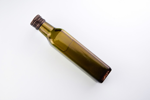 Green transparent glass bottle of olive oil on a light background.