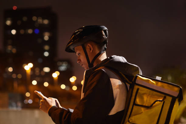 delivery rider at dusk looking at the smartphone. - bicycle messenger imagens e fotografias de stock