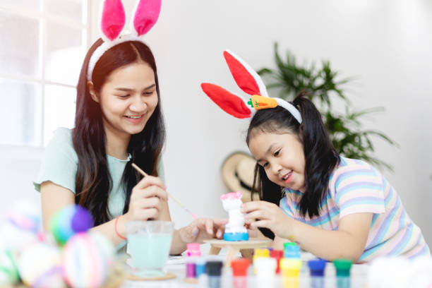 Asian kindergarten school girl with mother painting Plaster doll with Acrylic water color paint in living room at home. Homeschooling and distance learning. stock photo