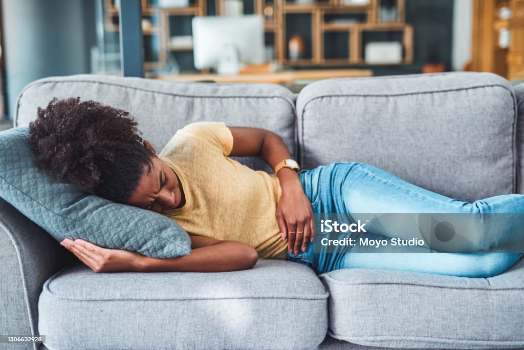 Tummy pain might be trying to tell you something Shot of a young woman experiencing stomach pain while lying on the sofa at home Endometriosis Stock Photo
